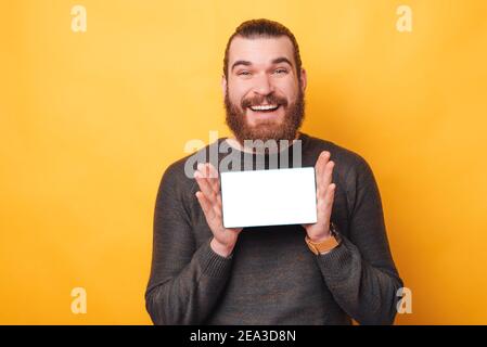 Portrait of amazed handsome man wearing sweater and showing blank screen on tablet over yellow background. Stock Photo