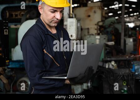 Skillful factory worker working with laptop computer to do procedure checklist . Factory production line operator occupation quality control concept . Stock Photo