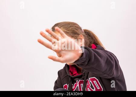 Young girl who denies being photographed shielding her face with hand in foreground Stock Photo