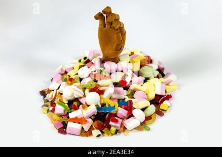 Save me from sugars! A wooden hand sticking out of a mountain of candies Stock Photo