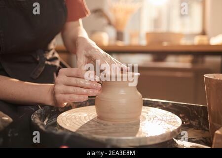 Warm toned closeup of female hands shaping clay on pottery wheel while making ceramics in sunlit workshop, copy space Stock Photo