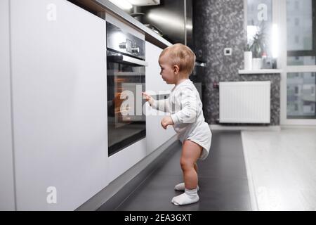 Infant baby boy near oven in home kitchen. Stock Photo