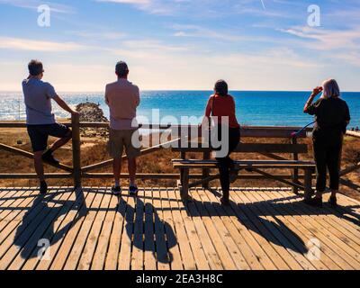 Marbella, Malaga, Spain.  October 2020.   Four tourists with their backs turned looking at the sea on a wooden viewing platform on the Marbella coastl Stock Photo