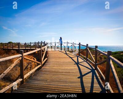 A young girl walking along a wooden walkway in front of the sea in Marbella on a sunny autumn day.