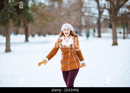 smiling elegant woman with mittens in a knitted hat and sheepskin coat outside in the city park in winter. Stock Photo