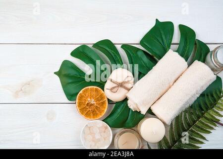 Bathroom accessories and a slice of orange on monstera leaves on a white wooden background. Stock Photo