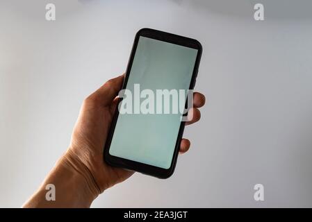 Woman hand holds smartphone with white screen. Female hand demonstrating new smartphone with blank screen Stock Photo