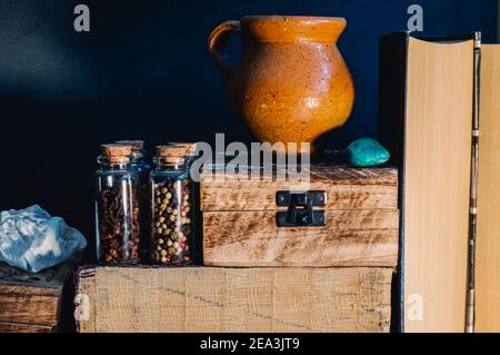 Still life image of books, wooden boxes, glass stopper bottles with spices an earthenware jug and semi precious stones in warm light