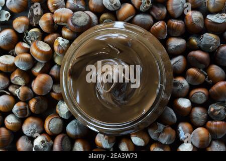 Vase with hazelnut praline paste and dry hazelnuts as background Stock Photo
