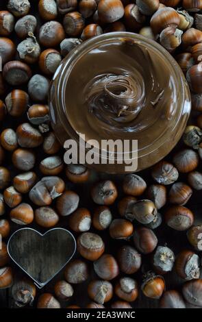 Vase with hazelnut praline paste ,heart shaped cutter and dry hazelnuts as background Stock Photo