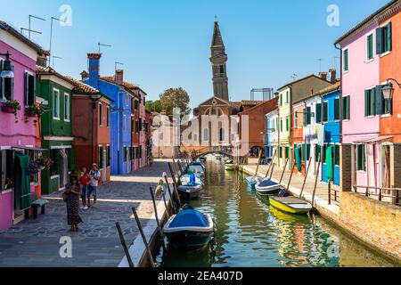 Burano, Italy, Sep. 2020 – A colorful canal in Burano whit the leaning bell tower of San Martino church in the background