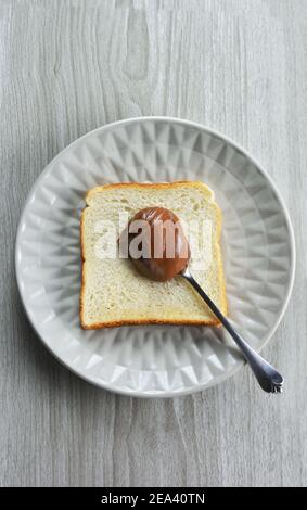 Slice of bread and spoonful of  hazelnut praline paste on a plate and grey table as background Stock Photo