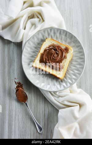Slice of bread spread with hazelnut praline paste on  a plate  and a spoon besides it Stock Photo