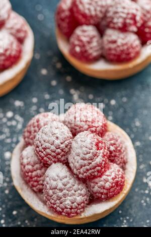 Set of appetizing raspberry tartlets with icing sugar on a spongy sponge base on a wooden table. Stock Photo