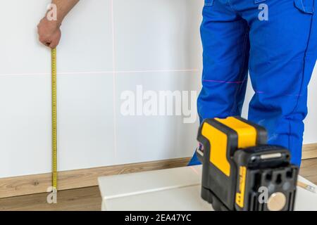 A specialist makes measurements on the wall with a measuring stick and an electronic laser to indicate levels and plumbs Stock Photo