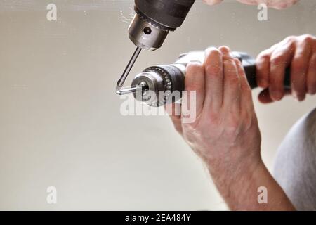 Worker drills hole in surface of mirror using glass drill bit. Stock Photo