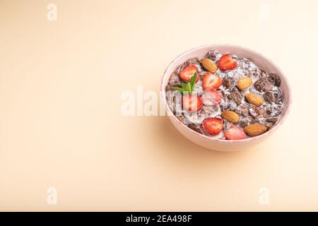 Chocolate cornflakes with milk, strawberry and almonds in ceramic bowl on pastel orange background. Side view, copy space. Stock Photo