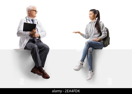 Full length shot of a female student talking to a mature doctor and sitting on a blank panel isolated on white background Stock Photo
