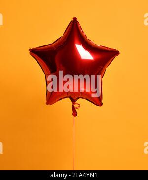 Single big red star metallic balloon ballon object for birthday party on dark yellow Stock Photo