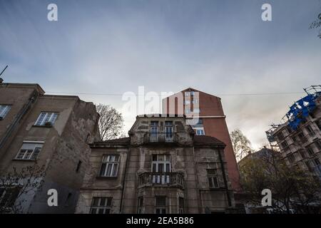 Old, neglected and decaying residential housing building surrounded by modern towers, some under construction, in a developping area of Belgrade, Serb Stock Photo