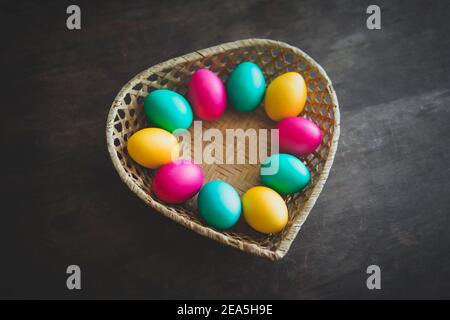 Easter eggs in basket on rustic wooden background. a basket made of straw in the form of a heart with colorful eggs painted for the holy orthodox Chri Stock Photo
