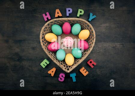 Happy Easter inscription on the wooden table. Easter Basket with colourful Eggs. Stock Photo