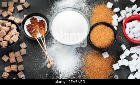 Different types of sugar: white, brown, cubes, powder, melted sugar candy. Dark background. Top view Stock Photo