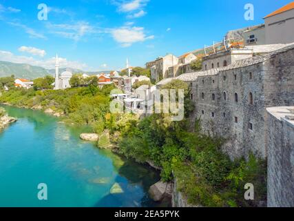 The river Neretva flows by the ancient wall surrounding the old town and village of Mostar, Bosnia and Herzegovina. Stock Photo