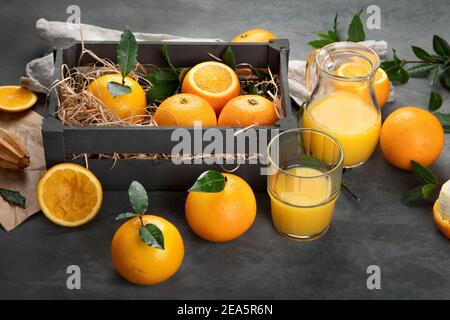 Oranges with leaves in wooden box, orange juice on dark grey background Stock Photo