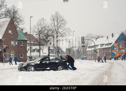 07 February 2021, North Rhine-Westphalia, Münster: A car is pushed out of the snow by helpers. Up to 30 centimetres of snow had fallen in East Westphalia and in Münsterland in the night to Sunday within a few hours. Photo: Ute Friederike Schernau/dpa Stock Photo