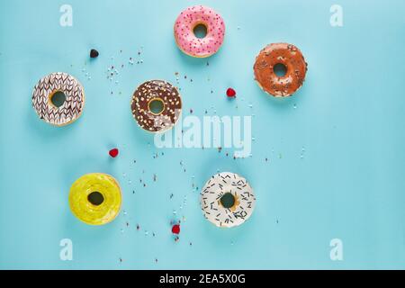 Multicolored donuts with frosting and sprinkles on blue background. Flat lay Stock Photo