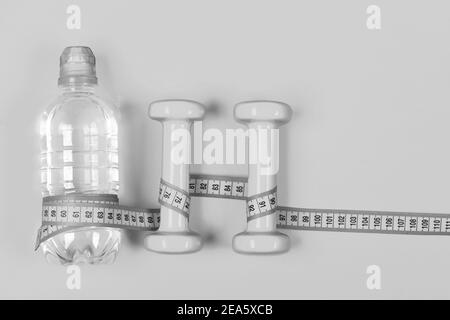 Centimeter wrapped around bottle and dumbbell, top view. Sports tools in cyan blue. Bottle of water and fitness equipment on yellow background. Shaping and refreshment concept. Stock Photo