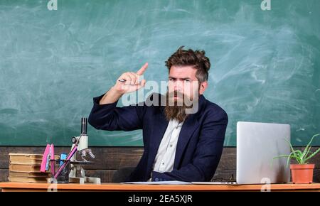 Teacher bearded man tell interesting story. Teacher charismatic hipster sit table classroom chalkboard background.Teacher interesting interlocutor as best friend. Telling educational stories. Stock Photo