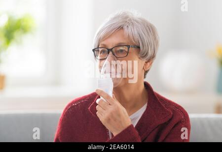 Elderly woman using inhaler for asthma and respiratory diseases at home. Stock Photo