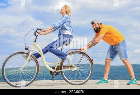 Learn cycling with support. Cycling technique. Woman rides bicycle sky background. How to learn to ride bike as adult. Girl cycling while boyfriend support her. Man helps keep balance and ride bike St...