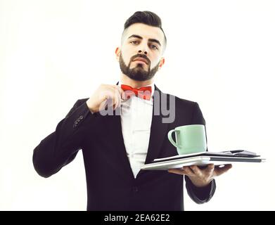 Businessman with beard, confident face and red bow tie checking it and holding notebook with cyan cup for tea, isolated on white background. Concept of importance, confidence and business break Stock Photo