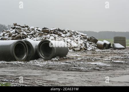 Broken and new concrete pipes for drainage installation on a construction site in the field on a wet and snowy day, selected focus, narrow depth of fi