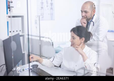 Young couple of doctors analysing medical scan on computer discovering the right treatment. Cardiologist showing and explaining results to his colleague using personal computer Stock Photo