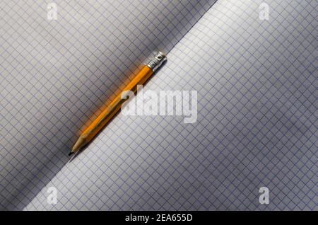 Engineering, accounting, business, education concept. Close-up of an old yellow wooden pencil on blank sheets of an open squared notebook. Selective f Stock Photo