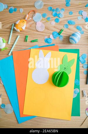 Flat lay with DIY paper Easter bunnies and colorful paper, easy crafts for kids. Stock Photo