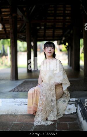 Portrait of Thai female with traditional Thai dress sitting with temple background Stock Photo