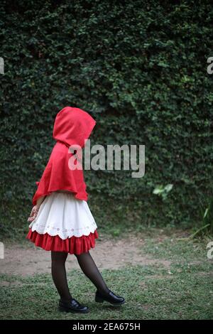 Portrait young woman with Little Red Riding Hood costume with apple and bread on basket in green tree park background Stock Photo