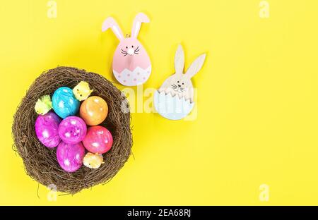 Easter eggs in nest and wooden decorative bunny on yellow background.  Stock Photo