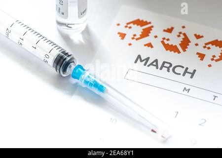 Syringe, glass vial or phial and calendar with month of March on a white table ready to be used. Covid or Coronavirus vaccine background, close up Stock Photo
