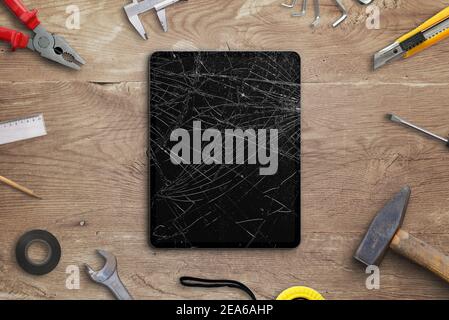 Repair broken tablet concept. Tablet with smashed disolay on work desk with tools beside. Top view, flat lay composition Stock Photo