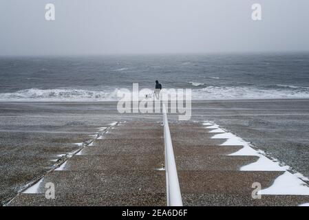 Man and his dog standing near the ocean during a blizzard in the Netherlands Stock Photo