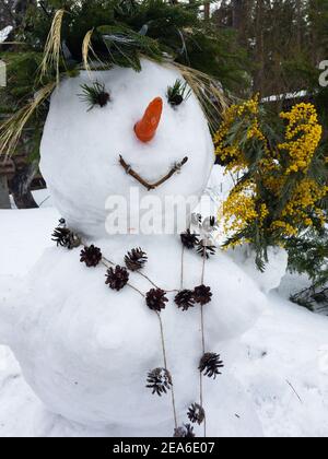 Snowman decorated with mimosa, beads, strobilus, carrot Stock Photo