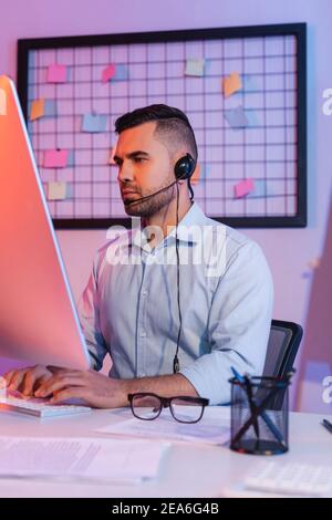 operator in headset typing on computer keyboard and looking at monitor Stock Photo