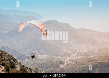A paraglider with an instructor and a student soars against the background of wooded mountains and hills Stock Photo