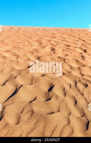 Close-up texture of the ridged surface of the sand with ripples and mini-dunes and blue sky in the desert during sunset. Stock Photo
